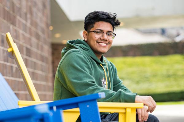 University of Rochester Student, 贾斯汀·皮门特尔，23岁, a computer science/history double major and first generation student from 的 Bronx, sitting on a yellow chair on campus.